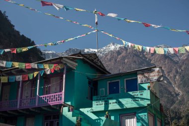 Annapurna pisti, Himalaya, Nepal, Asya 'da karla kaplı tepenin altında Budist bayrakları bulunan turkuaz çay evi.