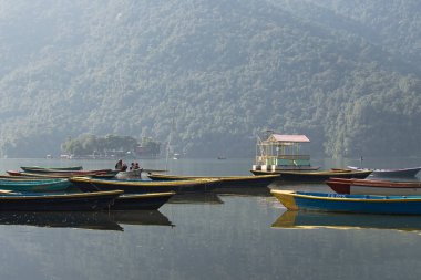 Pokhara, Nepal 'deki Phewa Gölü' nde arka planda dağlarla çevrili birkaç renkli tekneye bakın. Güneşli bir gün. Rahatlama ve sükunet, huzur ve sessizlik..