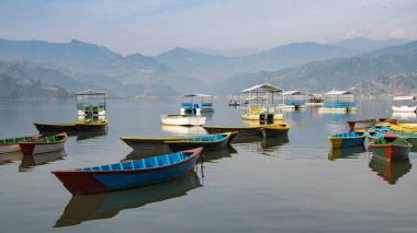 Pokhara, Nepal 'deki Phewa Gölü' nde arka planda dağlarla çevrili birkaç renkli tekneye bakın. Güneşli bir gün. Rahatlama ve sükunet, huzur ve sessizlik..