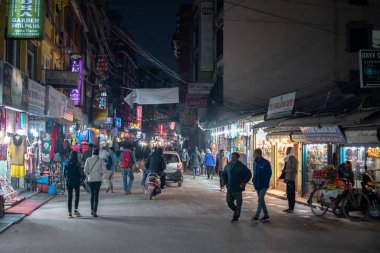 Thamel, Katmandu, Nepal - 22 Aralık 2019: Tanımlanamayan yayalar 22 Aralık 2019 'da Thamel, Katmandu, Nepal' de bir motosiklet ve bir araba geçerken geceleri dükkanları aydınlatarak yerel caddelerde yürürler