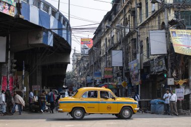 Kolkata, Hindistan - 1 Şubat 2020: Geleneksel sarı taksi 1 Şubat 2020 tarihinde Kolkata, Hindistan 'da Maa Flyover' ın altından geçerken, kimliği belirsiz insanlar sokakta ayakta ve yürüyor