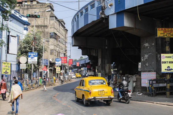Kolkata, Hindistan - 1 Şubat 2020: Geleneksel sarı taksi ve motosiklet Maa Flyover 'ın altından 1 Şubat 2020' de Hindistan 'ın Kolkata şehrinde geçerken, kimliği belirsiz insanlar sokakta yürüyor ve duruyor.