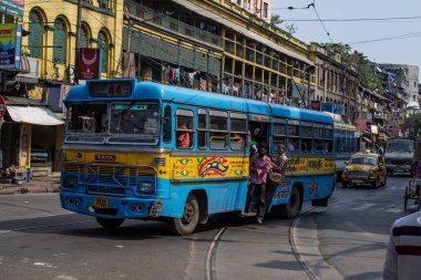 Kolkata, Hindistan - 2 Şubat 2020: Mavi ve sarı geleneksel toplu taşıma otobüsü 2 Şubat 2020 tarihinde Hindistan 'ın Kolkata kentinde, kimliği belirsiz bir tramvayın önünde ve sarı bir taksinin önünde.