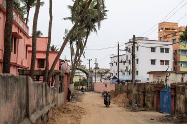 Puri, Hindistan - 3 Şubat 2020: Kimliği belirsiz insanlar 3 Şubat 2020 'de Puri, Hindistan' da apartman binalarının yanındaki küçük bir kırsal toprak yolda motosiklet sürüyor.