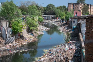 Chennai, Tamil Nadu, Hindistan 'ın gecekondu mahallelerindeki binalar ve ağaçlarla dolu plastik atıklarla dolu bir nehir.