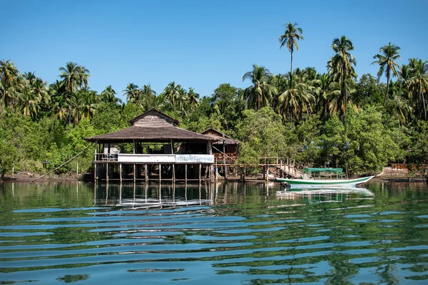 Bambu direkleri üzerinde küçük ahşap bir ev. Turkuaz nehir kıyısında, mangrov ve palmiye ağaçlarının yanında. Ngwesaung, Myanmar.