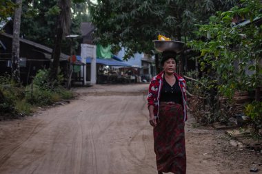 Chaung Thar, Myanmar - 26 Aralık 2019 Chaung Thar, Myanmar 'da kırsal bir kumda yürürken yerli bir kadın kafasında metal bir kase taşıyor.