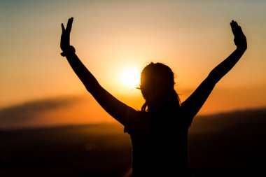 Gün batımında elleri havada bir kızın siluetinin görüntüsü 