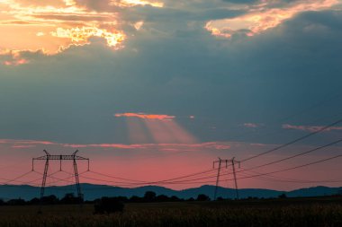Turuncu günbatımı gökyüzü arka plan ile alanda elektrik direkleri.