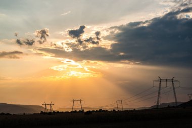 Turuncu günbatımı gökyüzü arka plan ile alanda elektrik direkleri.