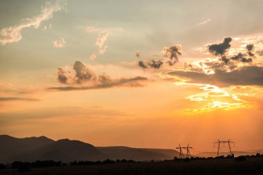 Turuncu günbatımı gökyüzü arka plan ile alanda elektrik direkleri.