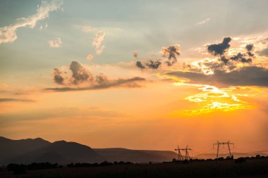 Turuncu günbatımı gökyüzü arka plan ile alanda elektrik direkleri.