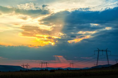 Turuncu günbatımı gökyüzü arka plan ile alanda elektrik direkleri.