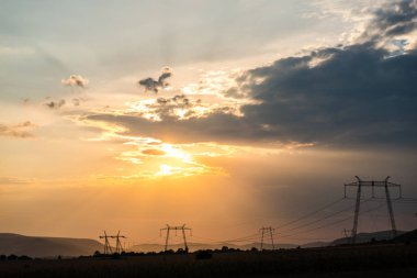 Turuncu günbatımı gökyüzü arka plan ile alanda elektrik direkleri.