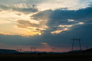 Turuncu günbatımı gökyüzü arka plan ile alanda elektrik direkleri.