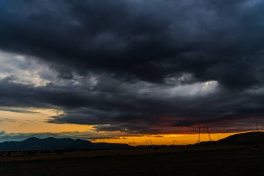 Turuncu günbatımı gökyüzü arka plan ile alanda elektrik direkleri.