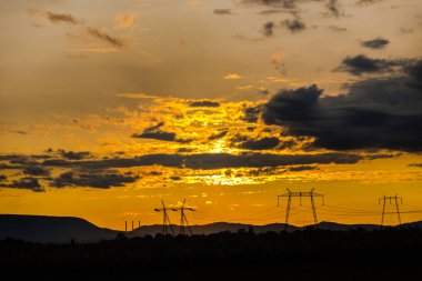 Turuncu günbatımı gökyüzü arka plan ile alanda elektrik direkleri.