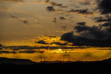 Turuncu günbatımı gökyüzü arka plan ile alanda elektrik direkleri.