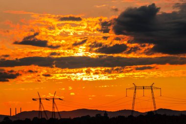 Turuncu günbatımı gökyüzü arka plan ile alanda elektrik direkleri.