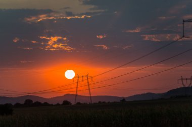 görkemli günbatımı gökyüzü dağlar siluet ufukta güneş ve elektrik direkleri,  