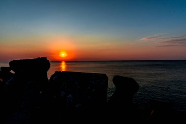 turuncu güneş ve deniz dalgakıran bloklarla günbatımı gökyüzü
