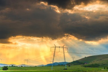 bulutlu gün batımı gökyüzü çayır çimen ve tepeler, alandaki elektrik direkleri ile yukarıda