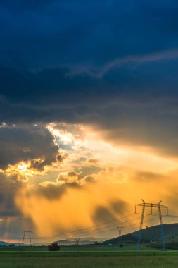 bulutlu gün batımı gökyüzü çayır çimen ve tepeler, alandaki elektrik direkleri ile yukarıda