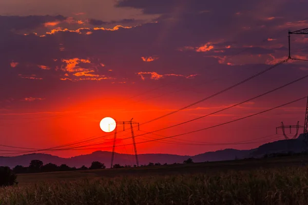bright red sun and sunset in sky, electric poles transmission
