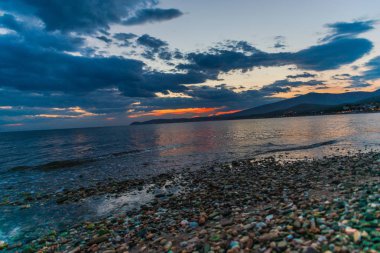 Sahil çakıl ve alacakaranlıkta sakin su ile