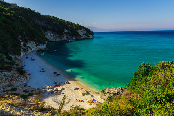 Tourists sunbathing at seashore in early morning, Greece.