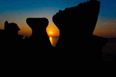 turuncu güneş ve deniz dalgakıran bloklarla günbatımı gökyüzü