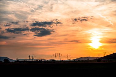kabloları ile turuncu günbatımı gökyüzü ve gerilim direkleri