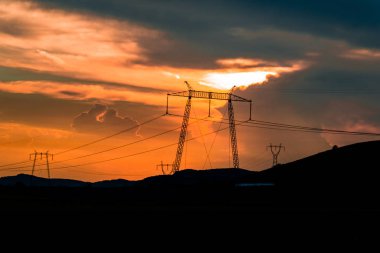 Elektrik direkleri ve gün batımı gökyüzü arka plan ile Alan