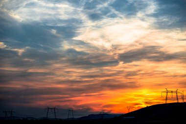 Günbatımı gökyüzü ve siyah elektrik direkleri siluetleri ile dramatik peyzaj