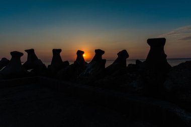 Dalgakıran bloklarla Okyanusu günbatımı gökyüzü turuncu güneşte