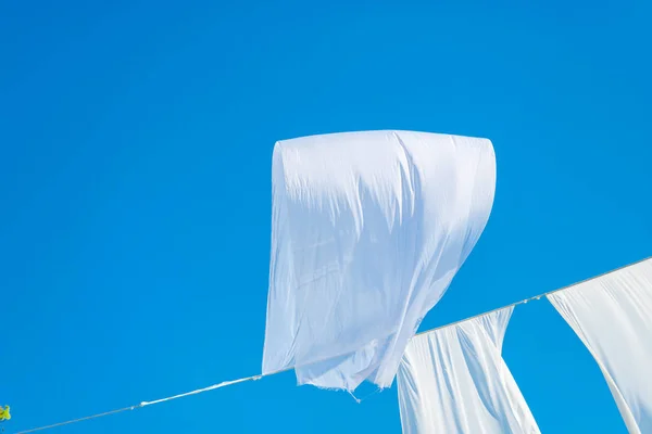 White waving curtains drying on thread line on blue sky background