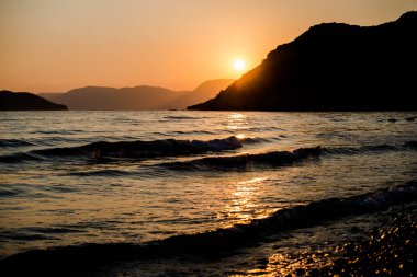 turuncu günbatımı gökyüzü güneş, dağlar ve deniz su yüzeyi ile akşam
