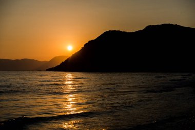 turuncu günbatımı gökyüzü güneş, dağlar ve deniz su yüzeyi ile akşam