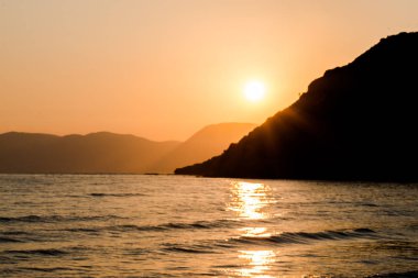 turuncu günbatımı gökyüzü güneş, dağlar ve deniz su yüzeyi ile akşam
