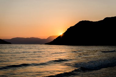 Arka planda dağlar gün batımında deniz kıyısı