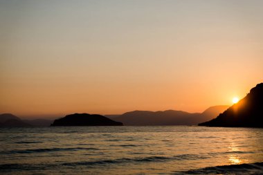 Arka planda dağlar gün batımında deniz kıyısı
