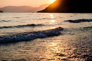 Arka planda dağlar gün batımında deniz kıyısı