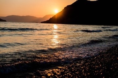 Arka planda dağlar gün batımında deniz kıyısı