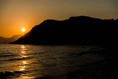 turuncu günbatımı gökyüzü güneş, dağlar ve deniz su yüzeyi ile akşam