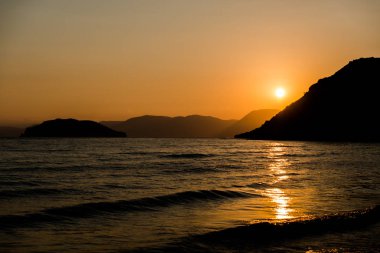 turuncu günbatımı gökyüzü güneş, dağlar ve deniz su yüzeyi ile akşam