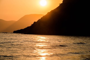 turuncu günbatımı gökyüzü güneş, dağlar ve deniz su yüzeyi ile akşam