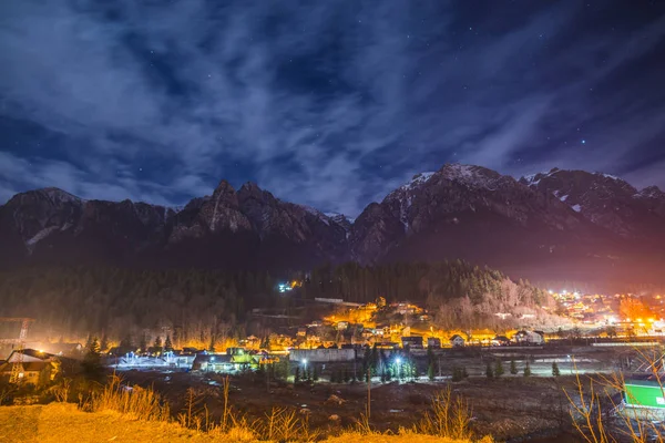 night sky with stars above mountains and illuminated houses in small village