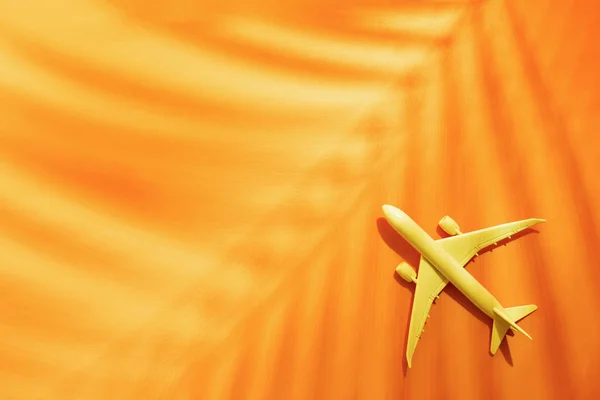 Model plane, airplane on orange color background with copy space and tropical palm leaf, — Stock Photo, Image