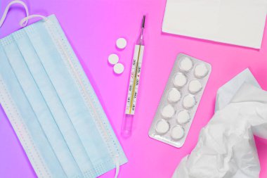 Tıbbi maskesi, mendiller, termometre ve ilaçlar mor pembe arka plan üzerinde. Soğuk algınlığı ve grip tedavisi kavramı. Boğaz ağrısı.