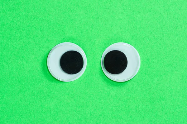 Cross-eyed googly eyes on neon green background. Mad funny toys eyes close up.